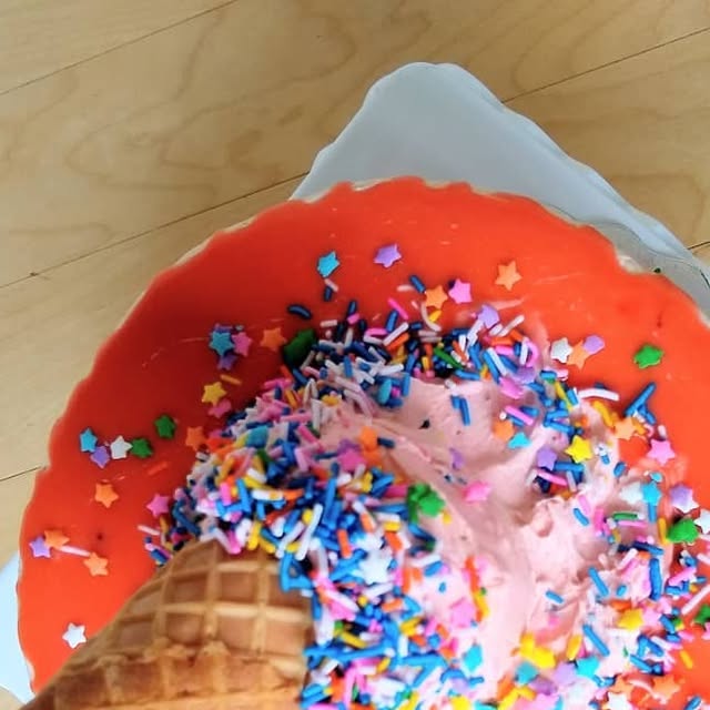 Cake sculpted like a tipped-over ice cream cone with pink drip and rainbow sprinkles